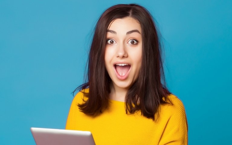 A young woman holding a tablet computer while looking surprised