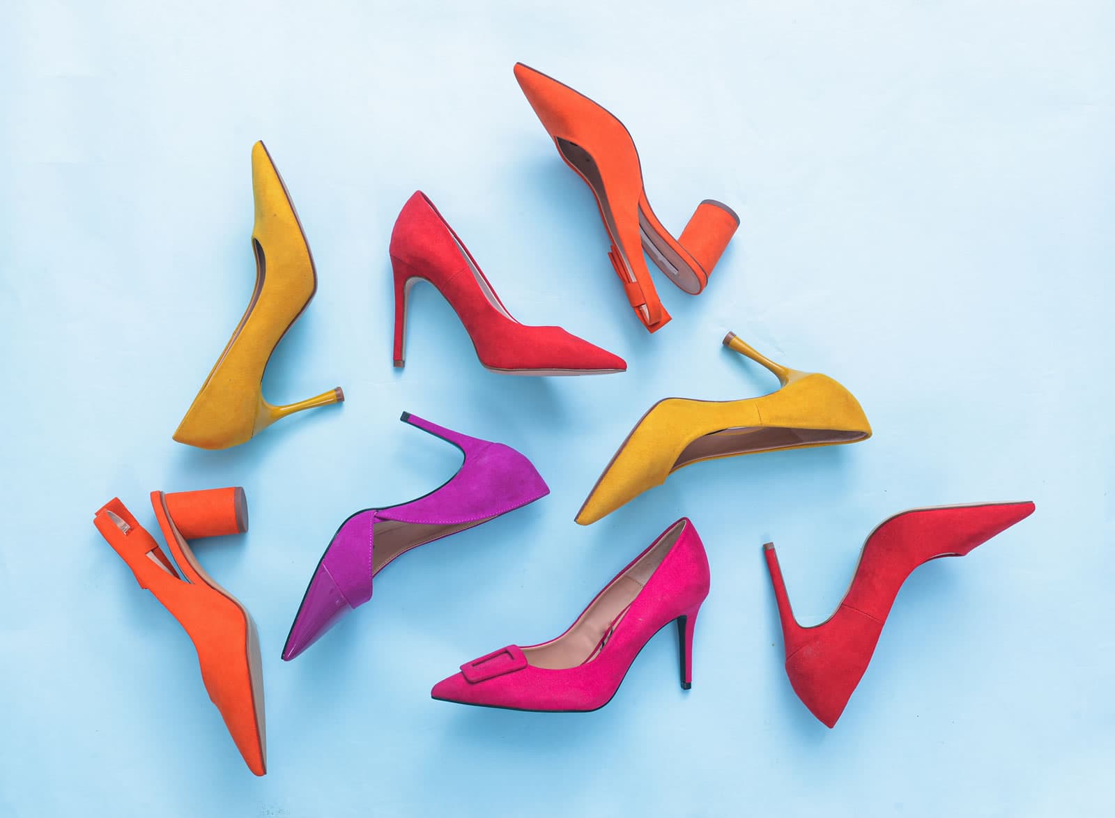 Arrangement of colouful women's high-heeled shoes in pink, orange, yellow, red and purple on blue background