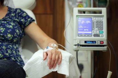 Female healthcare patient sat next to an infusion pump feeding an IV drip into her arm