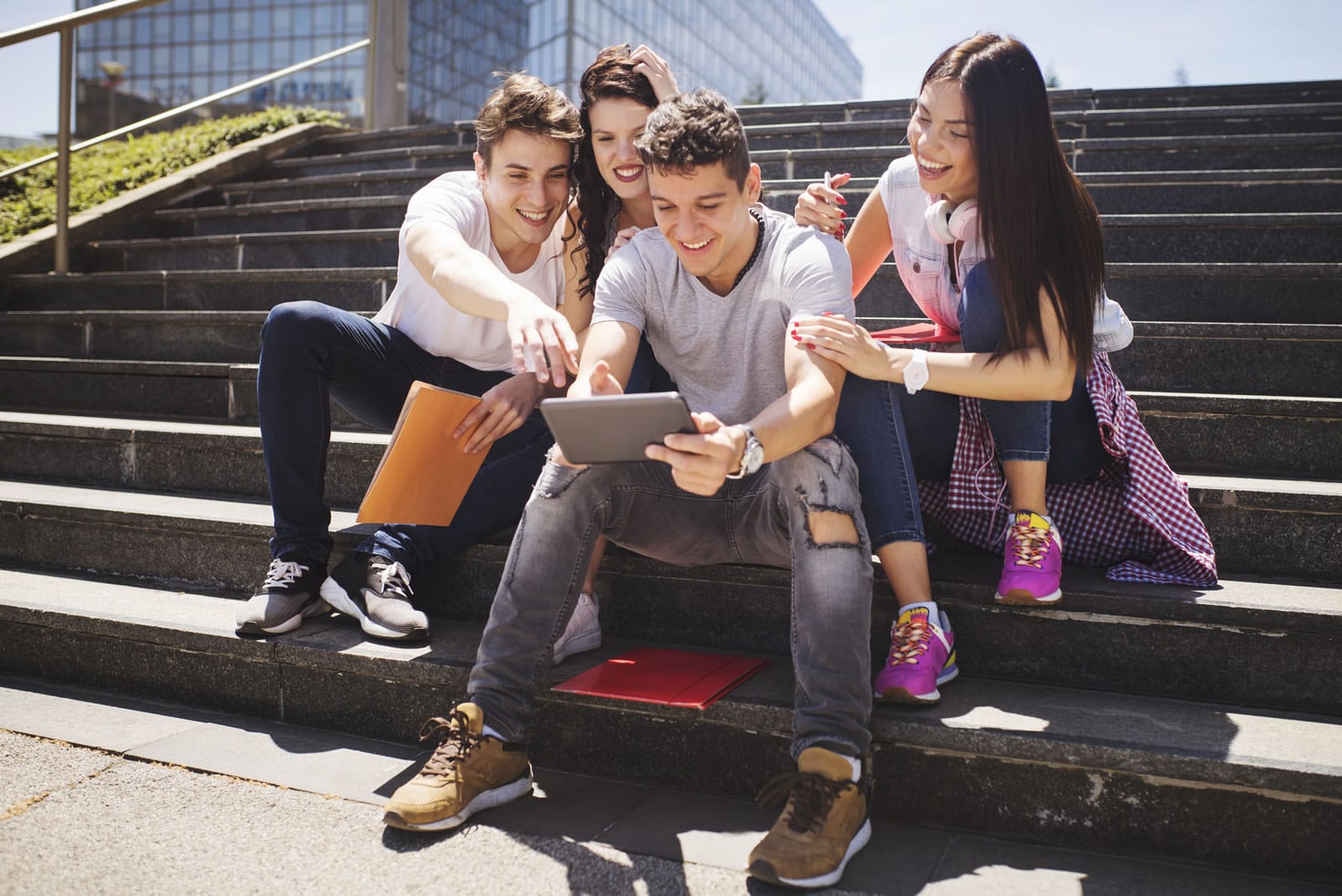 Four teenage friends in casual clothing sitting on steps smiling and laughing