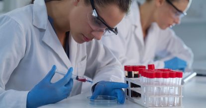 Two female lab technicians wearing personal protection equipment while handling medical samples in a lab