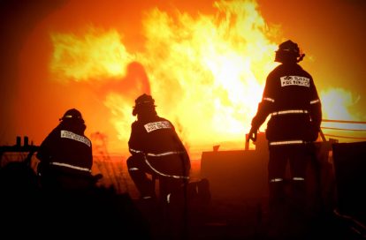 Volunteers from the New South Wales Rural Fire Service silhouetted in front of flames from an Australian bushfire