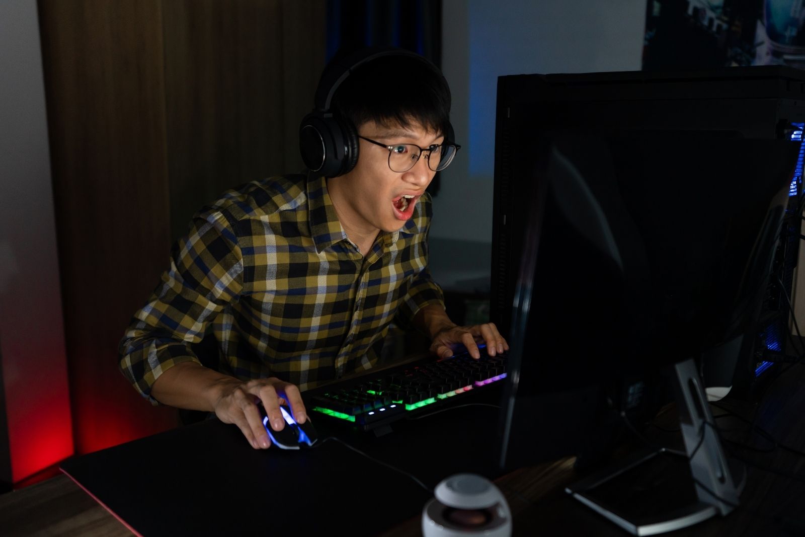 Asian teenager playing PC game in darkened room