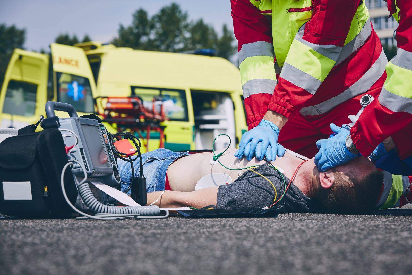 Two paramedics resuscitating an injured man lying in the road with his shirt off