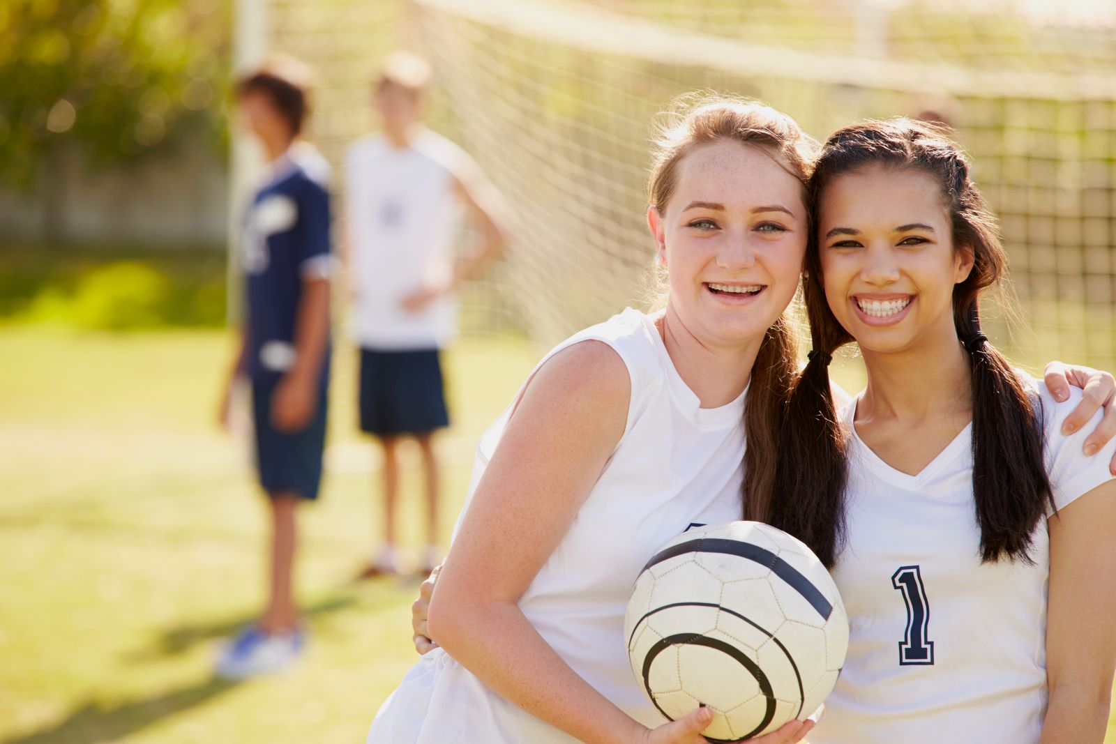 Two teenage girls smile for the camera while playing soccer