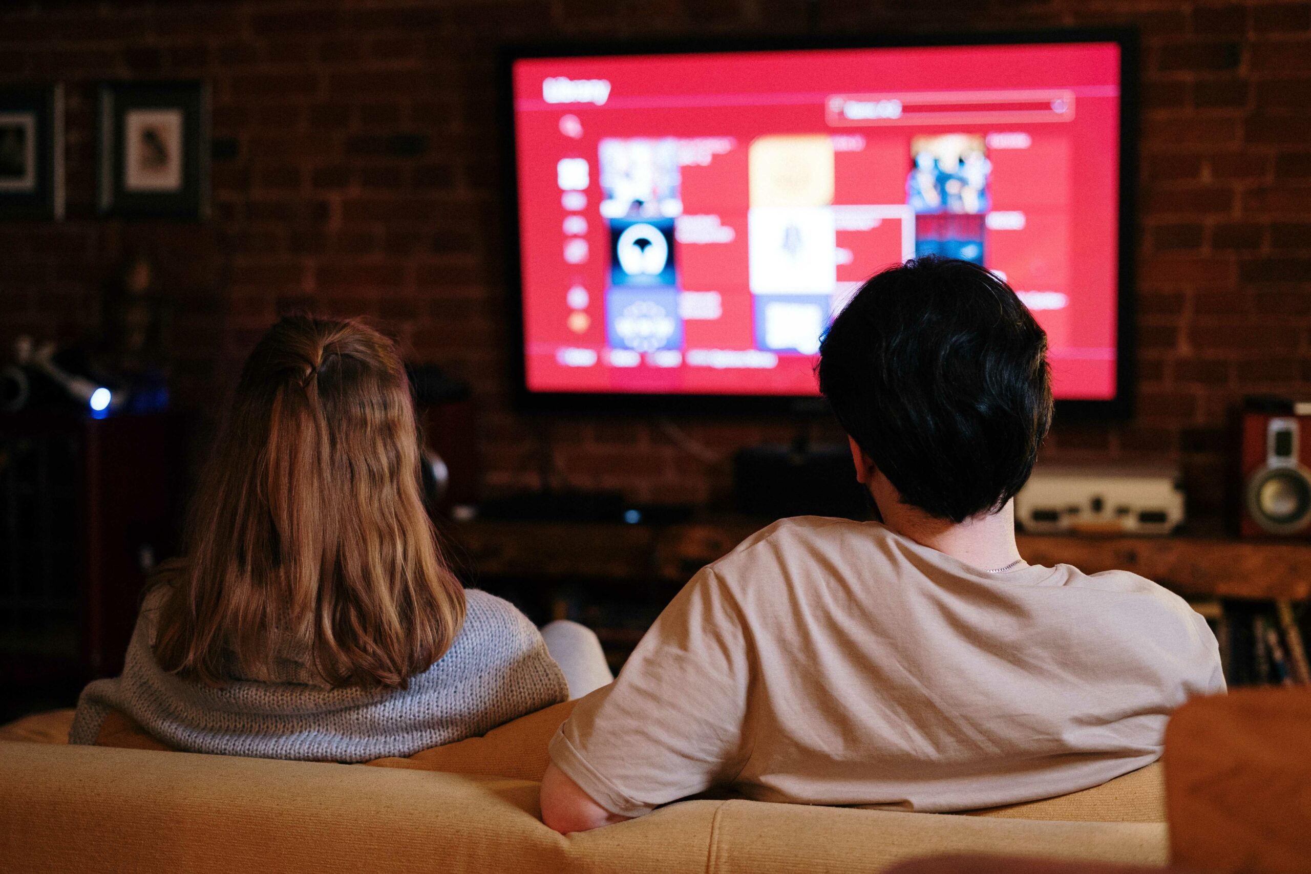 Couple on sofa using remote control to select which programme to stream on TV