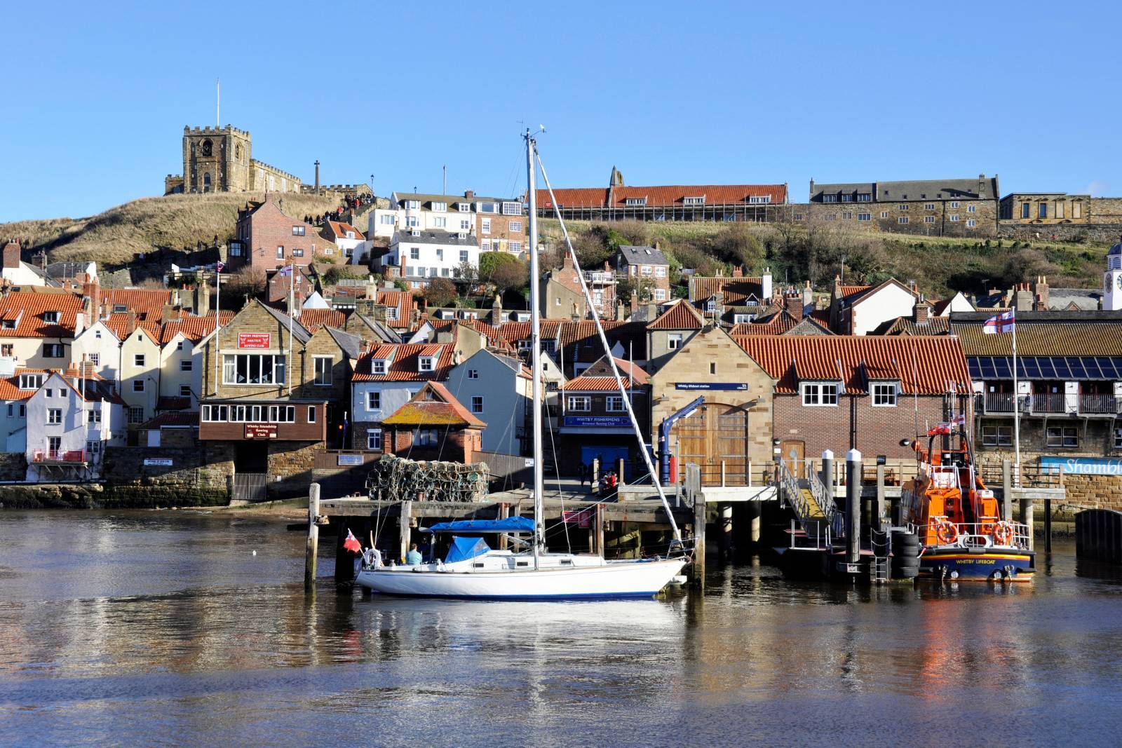 Whitby harbourfront on a sunny day lifeboat station and sailing yacht visible in the foreground