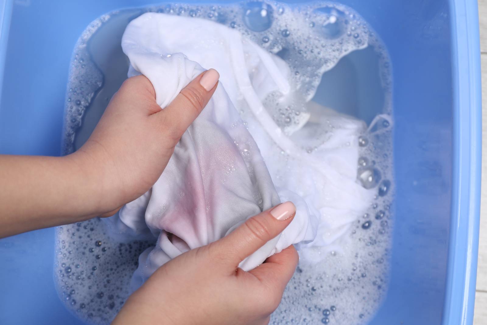 Woman using liquid stain remover on shirt in a bowl of soapy water