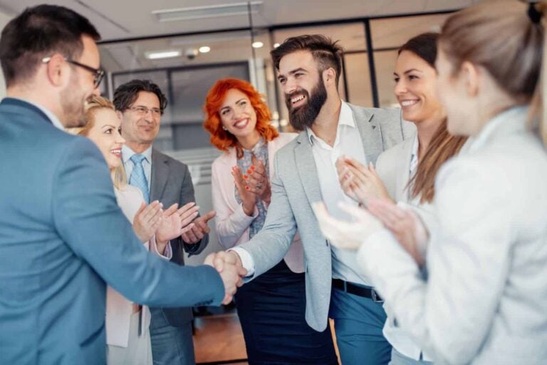 Concept of successful B2B market research success - two businessmen shake hands while colleagues clap