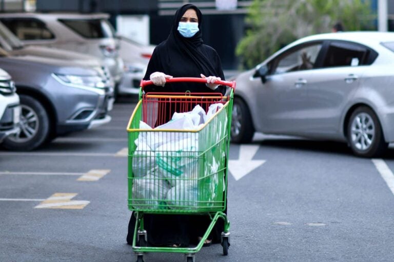 arab muslim woman pushing cart full of recycling outside supermarket in saudi arabia