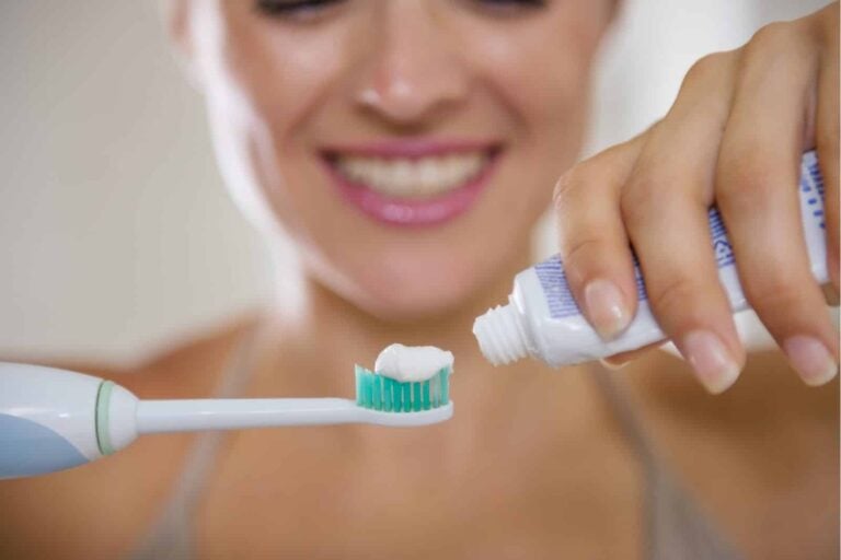 woman squeezing tube of toothpaste onto electronic toothbrush