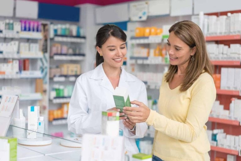 female customer discussing medication with pharmacist in well stocked pharmacy