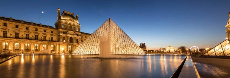 Paris, France - the Louvre Museum at sunset with the glass pyramid lit up in the centre and older buildings behind