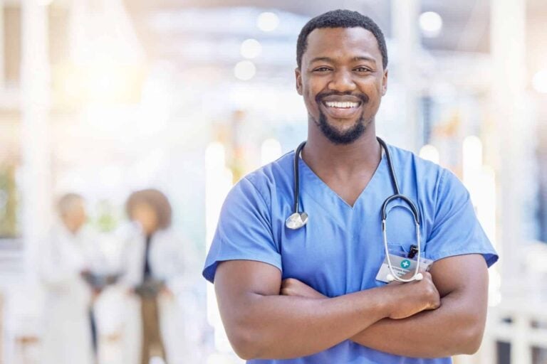 smiling male nurse in hospital corridor wearing scrubs with stethoscope around neck