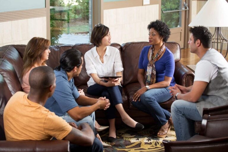A female moderator leads an informal focus group with five respondents in a relaxed living room setting