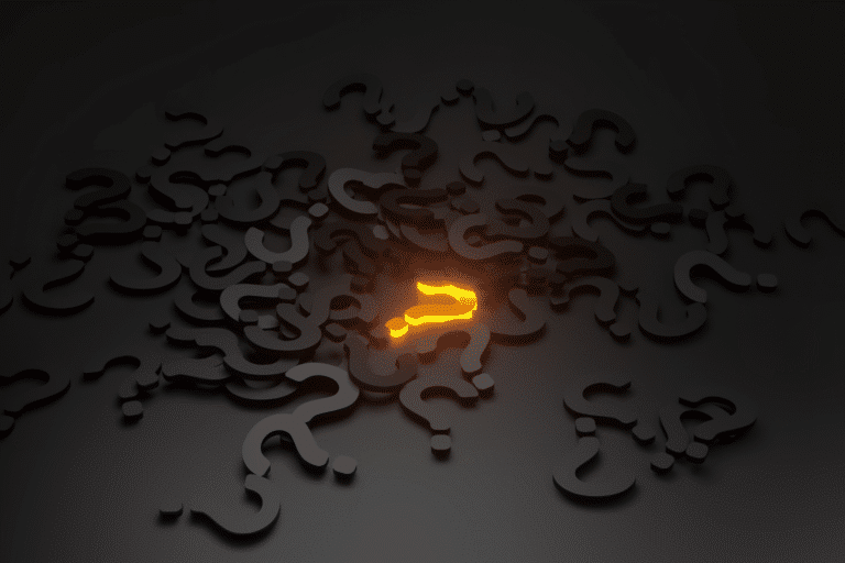 An illuminated question mark lying on a black desktop in a pile of black question marks