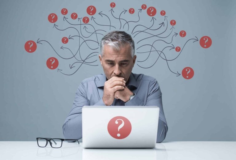 Plan for uncertain times concept - man sits at his desk looing at his laptop while surrounded by question marks