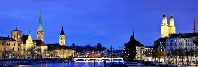 Zurich, Switzerland - panoramic view over the old town at night with the Limmat River in the foreground and several churches lit by floodlights