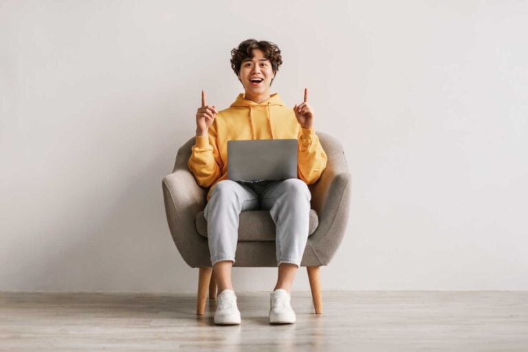 Millennial Asian man sits in an armchair and points upwards