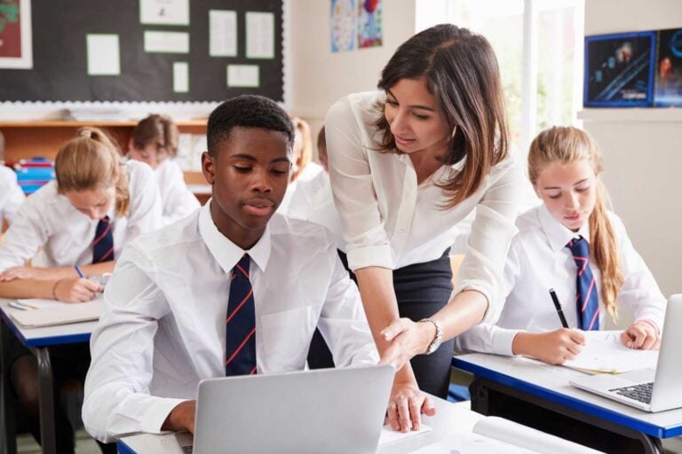 Teacher talking to a student with latop in a school classroom
