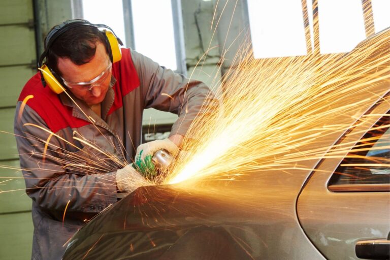 technician using angle grinder to repair car body in automotive workshop