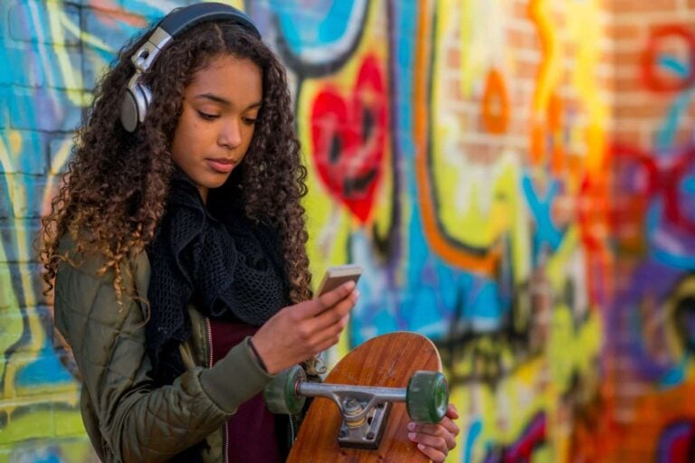 teenager with skateboard listening to streamed audio on headphones