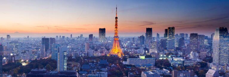 Tokyo, Japan - cityscape at dusk with tall buildings and the Tokyo Tower lit up in the centre. Mount Fuji is visible in the distance