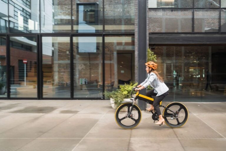Woman in casual wear riding an electric pedelec bike to go for work in city
