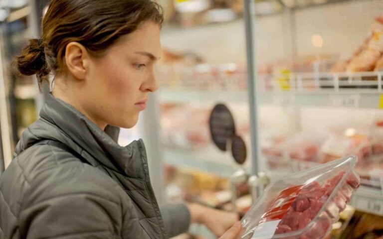 Woman reading label on pre-packed meat in a supermarket