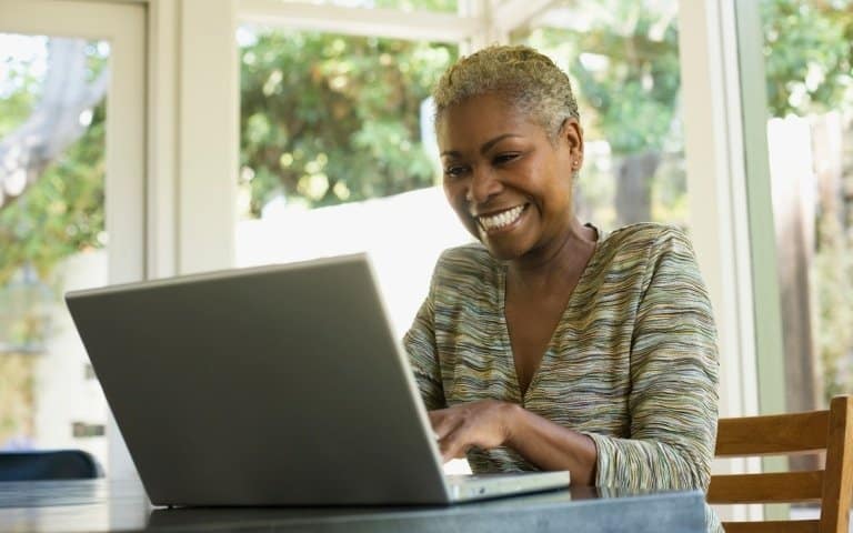 A black woman smiles as she types on a laptop computer at home during lockdown
