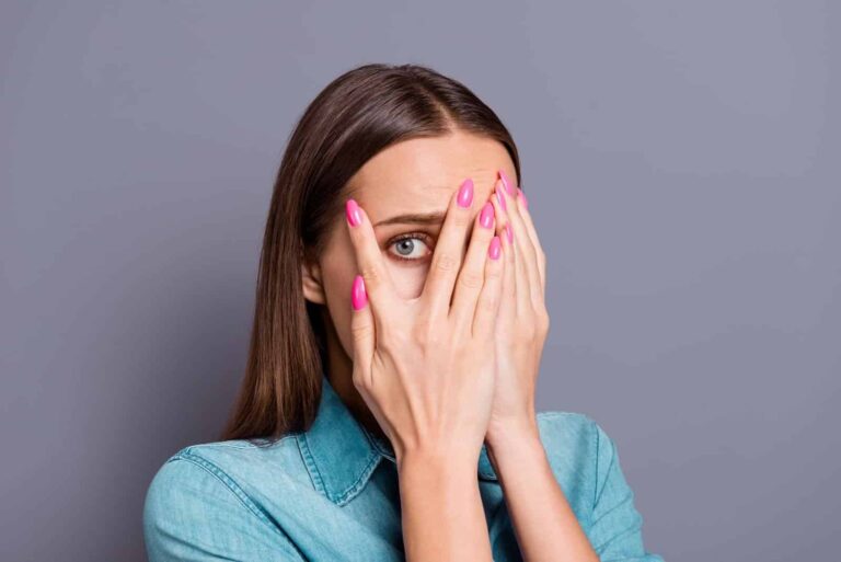 A young woman peeping from behind her hands and looking nervous