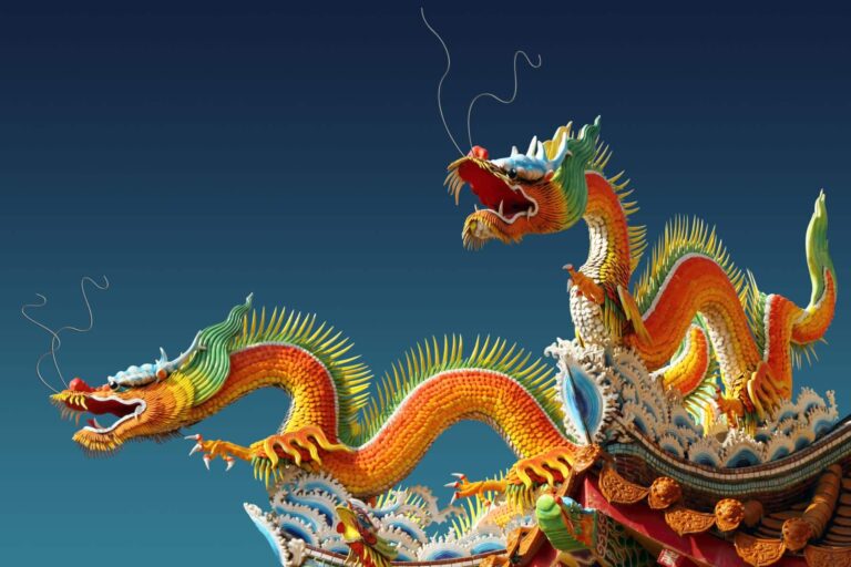 Two Chinese dragon ornaments on the roof of a temple against a clear blue sky