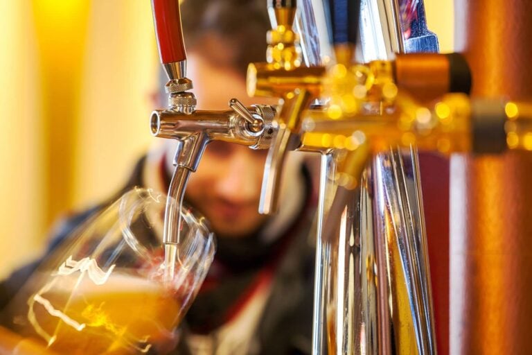 bartender pouring beer into a pint glass from a row of beer dispensers on tap