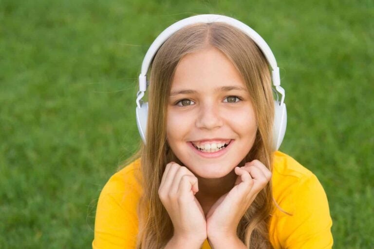 young girl listening to story on headphones outside lying on grass