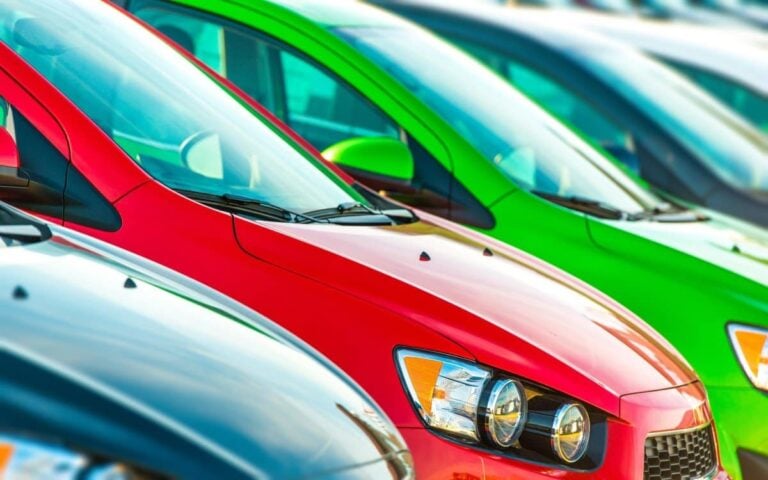 row of colourful new cars in black, red and green for sale in used car lot