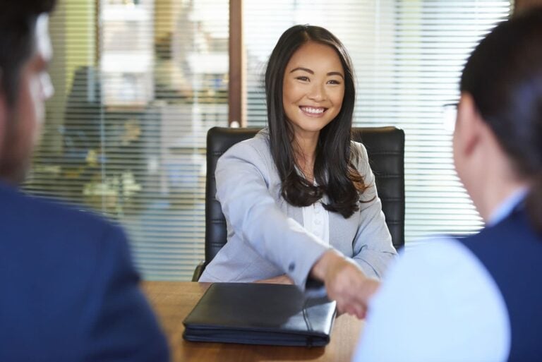 Female university applicant seated across from interviewer abd shaking hands as she completes an admissions interview