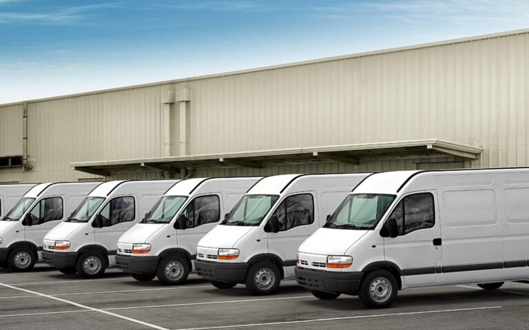 fleet of white vans parked outside a warehouse