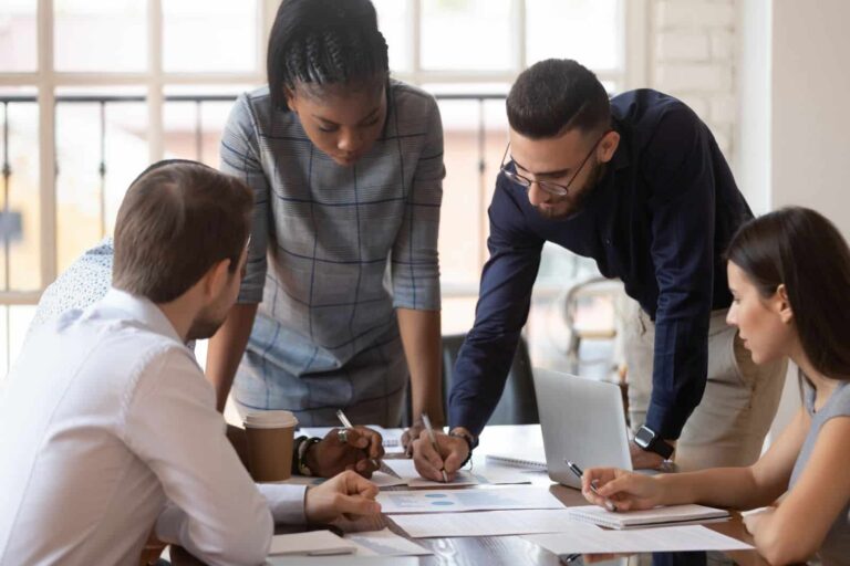 Focused multiracial team of corporate business people brainstorm on marketing plan financial report gather at office table meeting, diverse serious colleagues group discuss paperwork engaged in teamwork