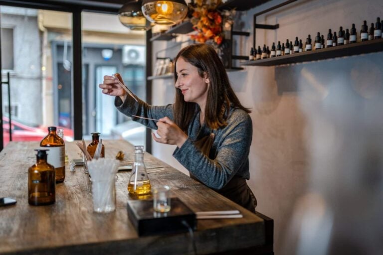 Young Perfumer preparing perfume while sitting at table in her own store