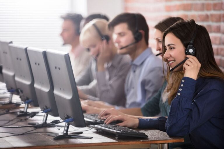 young call centre workers on a helpdesk while wearing headsets and reading script from computer