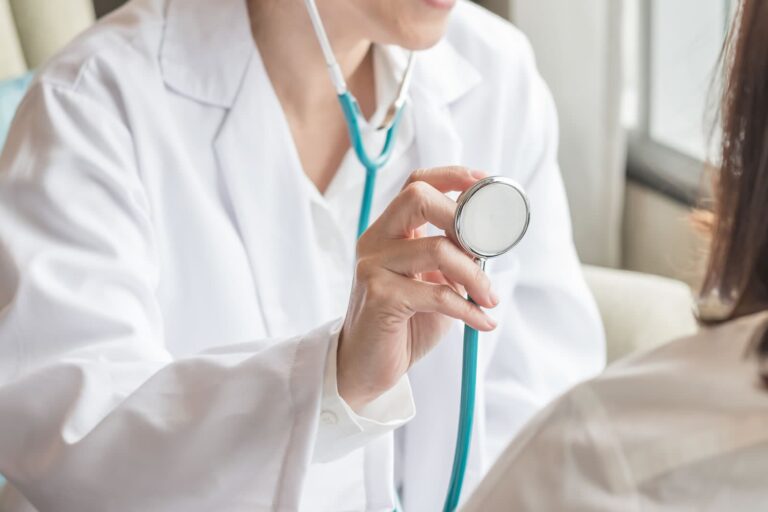 cardiologist healthcare professional holds stethoscope towards patient during check up