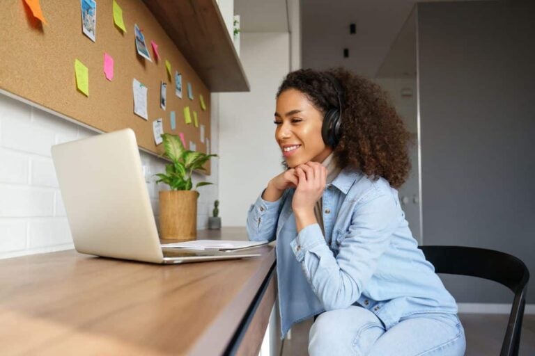 A young female moderator sits in front of her laptop at her home office desk, reviewing submission to an online bulletin board