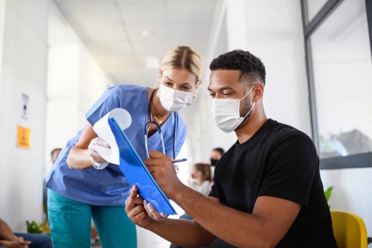 Patient wearing facemask signs insurance form for doctor