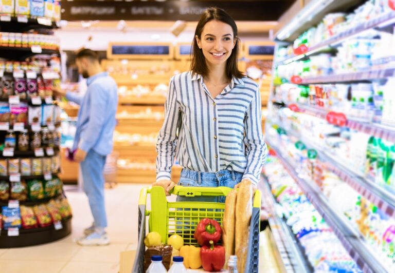 woman shopping in grocery section of department store with cart of food and beverages