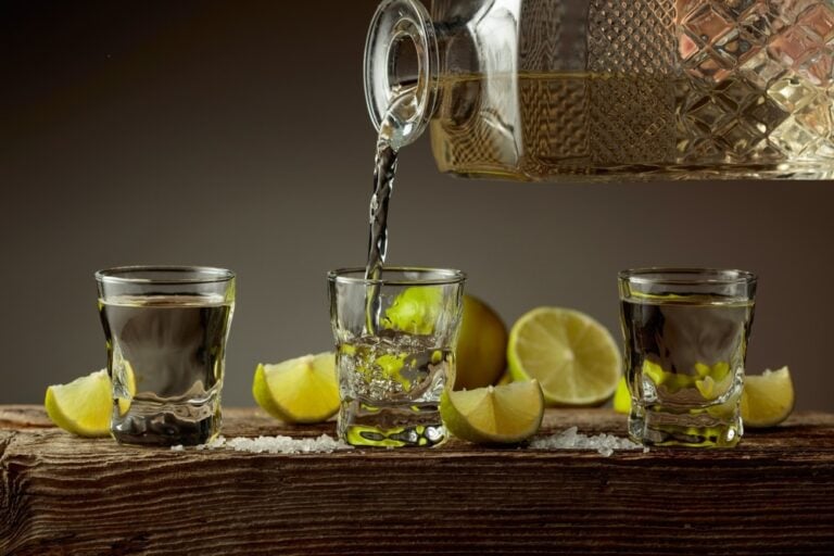 bottle of premium tequila with salt and limes poured into glass on old wooden board