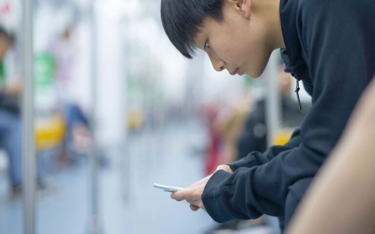 teenage boy sitting on public transport using smartphone to access social media platform