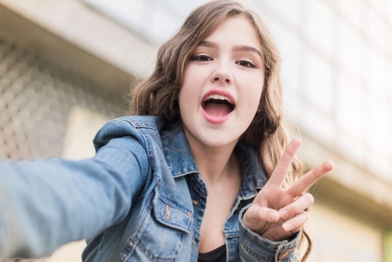 teenager making peace sign with hand while holding smartphone to make selfie video to post online on snap!