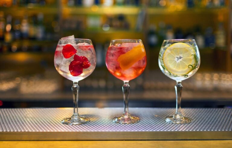 Three cocktails with a bar and liquor bottles in the background