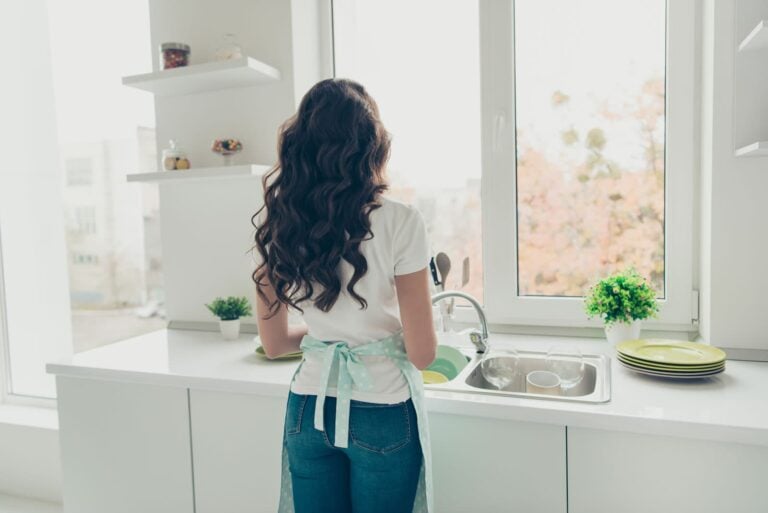 Woman testing medical packaging at kitchen sink viewed from behind
