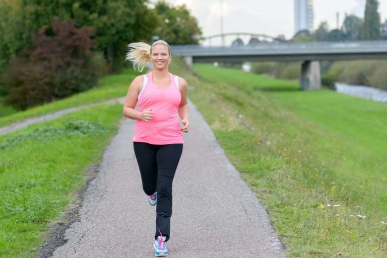 young female in pink and black sportswear running on a path alongside a river